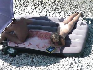 Парень и девушка на нудистском пляже плавают на матрасе