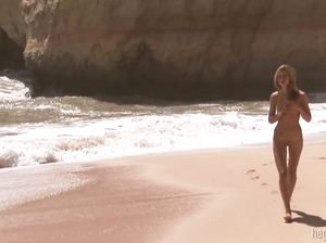 Обнаженная блондинка резвится на пляже и загорает на горячем песке