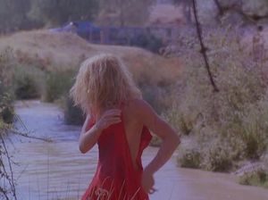 Голая блондинка стирает платье в реке