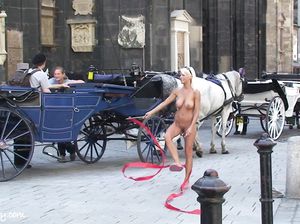 Голая девушка позирует посреди площади у красивой кареты